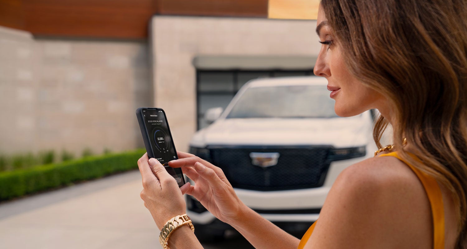 lady checking her mobile with a Cadillac vehicle background | Cadillac of Jackson in Ridgeland MS